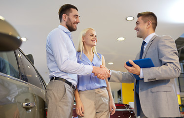 Image showing happy couple with car dealer in auto show or salon