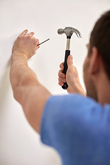 Image showing close up of man with hammer hammering nail in wall