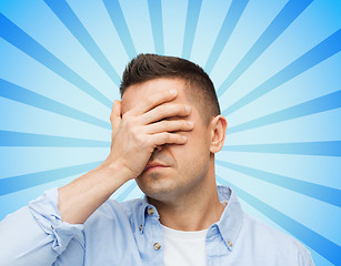 Image showing unhappy man covering his eyes by hand