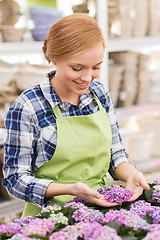 Image showing happy woman taking care of flowers in greenhouse