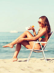 Image showing smiling young woman sunbathing in lounge on beach