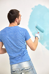 Image showing man with roller painting wall in blue at home