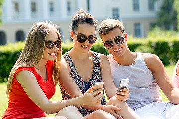 Image showing smiling friends with smartphones sitting in park