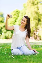 Image showing smiling young girl with smartphone sitting in park