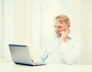 Image showing old man in eyeglasses working with laptop at home