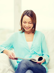 Image showing smiling woman reading magazine at home