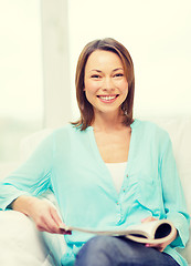 Image showing smiling woman reading magazine at home