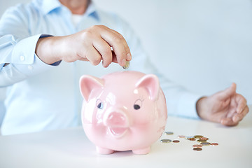 Image showing close up of old man putting coins into piggybank