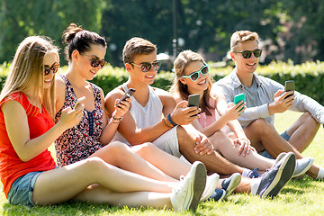 Image showing smiling friends with smartphones sitting on grass