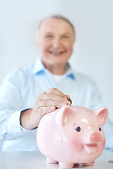 Image showing close up of old man putting coin into piggybank