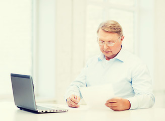 Image showing old man in eyeglasses filling a form at home