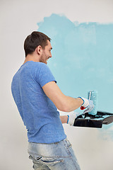 Image showing happy man with roller painting wall at home