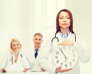 Image showing calm female doctor with wall clock