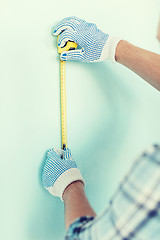 Image showing closeup of male in gloves measuring wall with tape