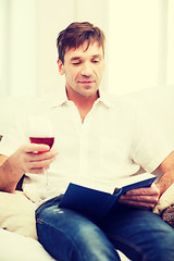 Image showing happy man with book and glass of rose wine at home