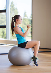 Image showing smiling woman with dumbbells and exercise ball