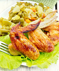 Image showing Chicken wings fried with vegetables in plate on board