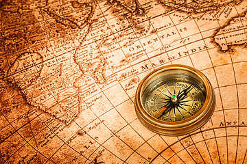 Image showing Vintage compass lies on an ancient world map.