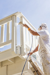 Image showing House Painter Spray Painting A Deck of A Home