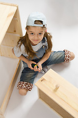 Image showing Little girl in overalls collector furniture spins screwdriver