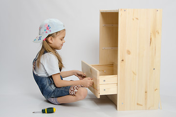Image showing Girl in overalls furniture collector tries to insert drawer a chest of drawers