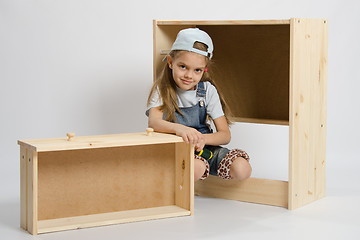 Image showing Little girl in overalls sits beside the garbage furniture elements Chest