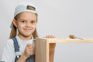 Image showing Girl in overalls furniture collector tries to tighten the screw