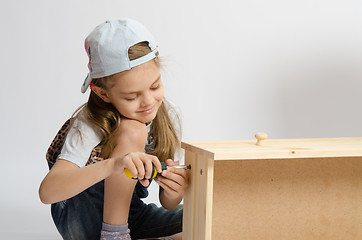 Image showing Little girl in overalls collector of furniture screws screwdriver screw