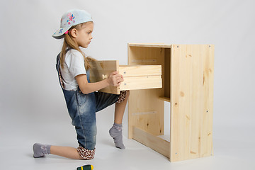Image showing Girl in overalls furniture assembler inserts a drawer chest of drawers