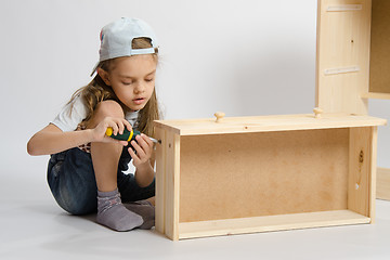 Image showing Little girl in overalls collector of furniture making box on the dresser