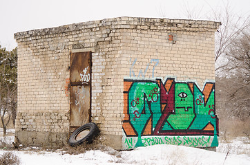 Image showing old one-story brick building a rusty door with graffiti on wall