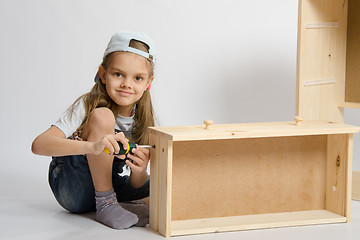 Image showing Little girl in overalls collector collects furniture drawer of the dresser