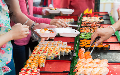 Image showing close up of hands with tongs taking sushi