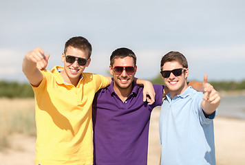 Image showing smiling friends in sunglasses showing thumbs up