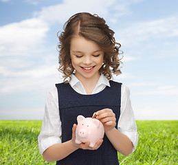 Image showing happy girl putting coin into piggy bank