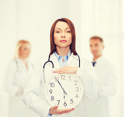 Image showing calm female doctor with wall clock