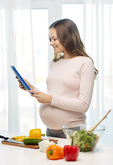 Image showing happy pregnant woman with tablet pc cooking food