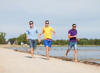 Image showing smiling friends in sunglasses running along beach