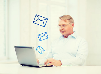 Image showing old man in eyeglasses working with laptop at home