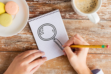 Image showing close up of hands drawing magnifier in notebook