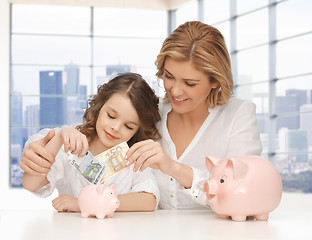 Image showing mother and daughter putting money to piggy banks