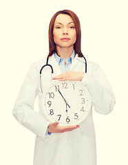 Image showing calm female doctor with wall clock