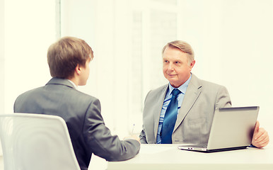 Image showing older man and young man signing papers in office