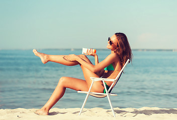 Image showing smiling young woman sunbathing in lounge on beach