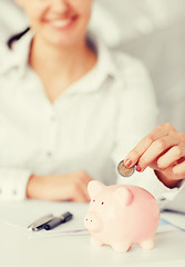 Image showing woman hand putting coin into small piggy bank