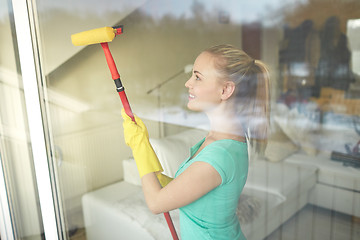 Image showing happy woman in gloves cleaning window with sponge