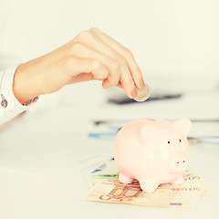 Image showing woman hand putting coin into small piggy bank