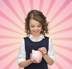 Image showing happy girl putting coin into piggy bank