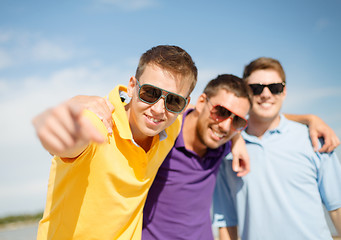 Image showing smiling friends in sunglasses pointing at you