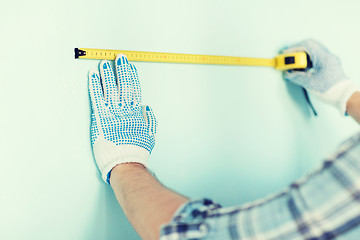 Image showing closeup of male in gloves measuring wall with tape